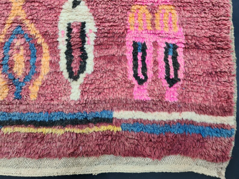 May include: Close-up of a pink, white, blue, and orange patterned rug with a fringe border. The rug has a textured, woven look.