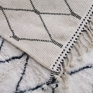 May include: Two white rugs with black geometric patterns. The top rug has a fringe border and a diamond pattern. The bottom rug has a more intricate pattern.