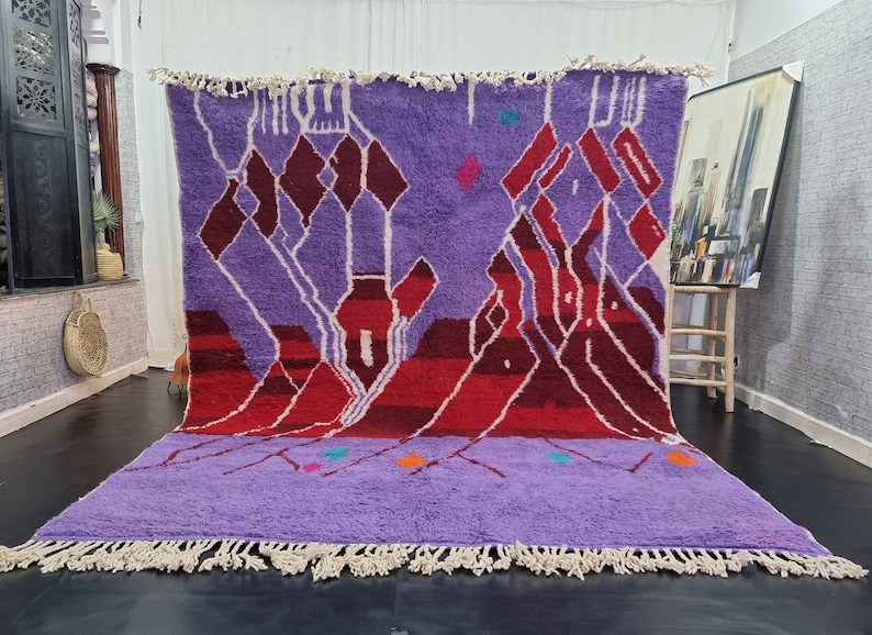 May include: A purple and red Moroccan rug with a geometric pattern. The rug has a fringe border and is made of wool.