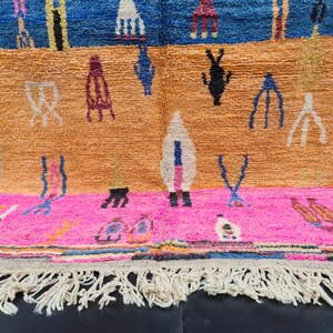 May include: A colorful Moroccan rug with a geometric pattern in shades of blue, orange, pink, and white. The rug has a fringe border and is made of wool.