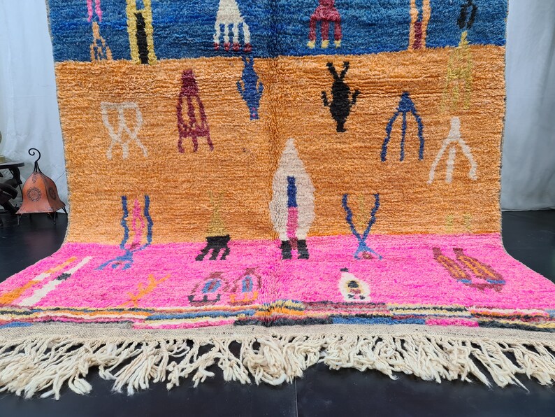 May include: A colorful Moroccan rug with a geometric pattern in shades of blue, orange, pink, and white. The rug has a fringe border and is made of wool.