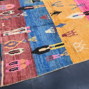 May include: A colorful Moroccan rug with a geometric pattern in shades of pink, blue, orange, and white. The rug has a fringe border and is made of wool.
