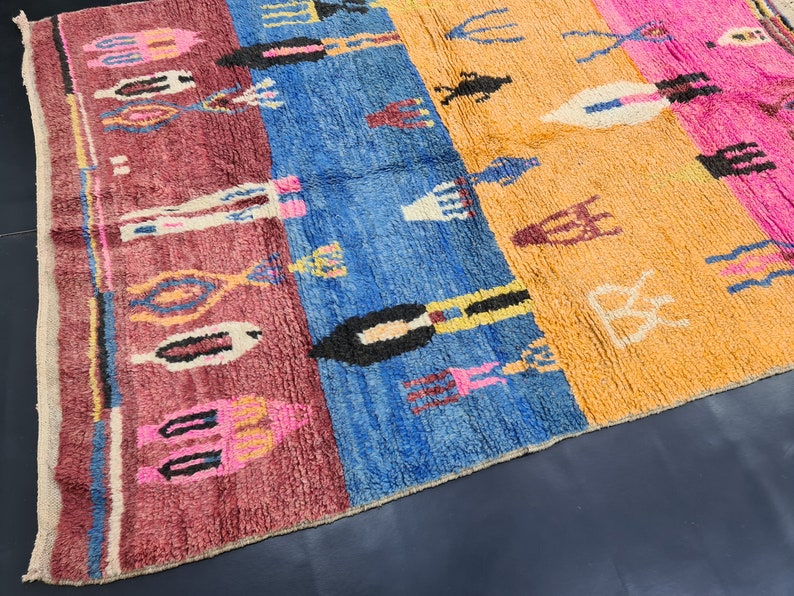 May include: A colorful Moroccan rug with a geometric pattern in shades of pink, blue, orange, and white. The rug has a fringe border and is made of wool.