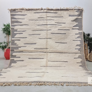 May include: A white and gray Moroccan rug with a geometric pattern. The rug has a fringe border and is made of wool.