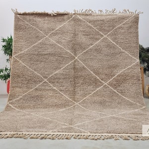 Puede incluir: Una alfombra marroquí beige con un patrón de diamantes tejido en la tela. La alfombra tiene un borde de flecos.