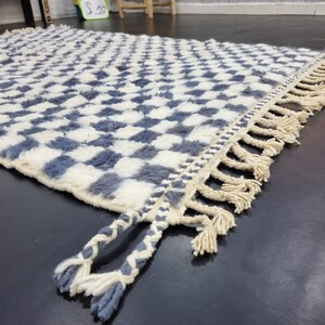 Op de afbeelding: Een wit en blauw geruit tapijt met een franje rand. Het tapijt is gemaakt van een zacht, pluche materiaal.