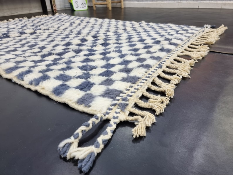 Op de afbeelding: Een wit en blauw geruit tapijt met een franje rand. Het tapijt is gemaakt van een zacht, pluche materiaal.