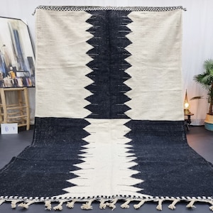 Puede incluir: Alfombra geométrica con patrón blanco y negro con flecos. La alfombra tiene un patrón de diamante con triángulos blancos y negros.