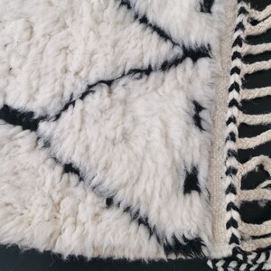 May include: White and black rug with a geometric pattern and fringe. The rug is made of a soft, fluffy material.