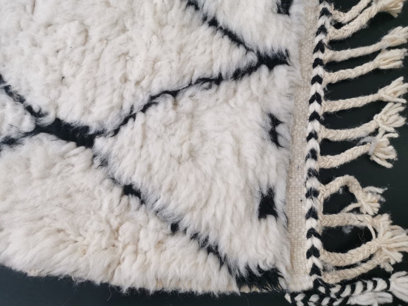 May include: White and black rug with a geometric pattern and fringe. The rug is made of a soft, fluffy material.