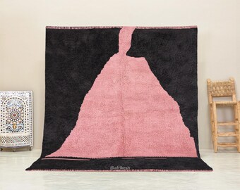 Könnte beinhalten: Ein marokkanischer Teppich in Schwarz und Rosa mit einem einzigartigen abstrakten Design. Der Teppich hat einen schwarzen Rand und eine rosa Mitte mit schwarzem Umriss. Der Teppich ist aus Wolle und handgewebt.