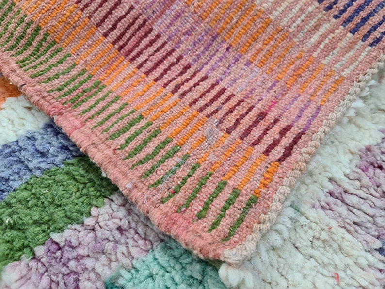 May include: Two woven rugs with a colorful striped pattern. The top rug is pink, orange, green, and purple. The bottom rug is white, green, purple, and blue.
