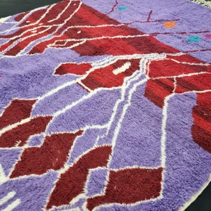 May include: A purple and red Moroccan rug with a geometric pattern. The rug has a white fringe around the edges.