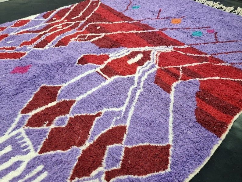 May include: A purple and red Moroccan rug with a geometric pattern. The rug has a white fringe around the edges.