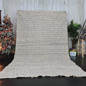 Puede incluir: Una alfombra grande, rectangular, de rayas blancas y grises con un borde de flecos. La alfombra est&aacute; colocada sobre un suelo oscuro en una habitaci&oacute;n con un &aacute;rbol de Navidad y otras decoraciones.