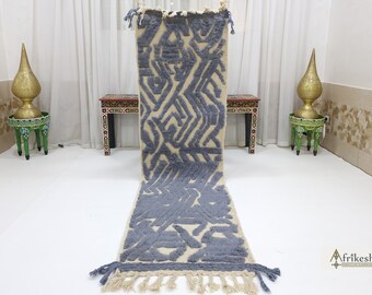 May include: A gray and white geometric patterned runner rug with fringe on the ends. The rug is laying flat on a white floor.