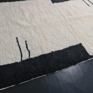 May include: A white rug with black geometric designs. The rug has a fringe border.
