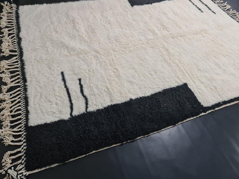 May include: A white rug with black geometric designs. The rug has a fringe border.