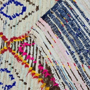 May include: A close-up of a colorful Moroccan rug with a white background and a variety of colors including blue, pink, yellow, and red. The rug is made of wool and has a hand-woven texture.