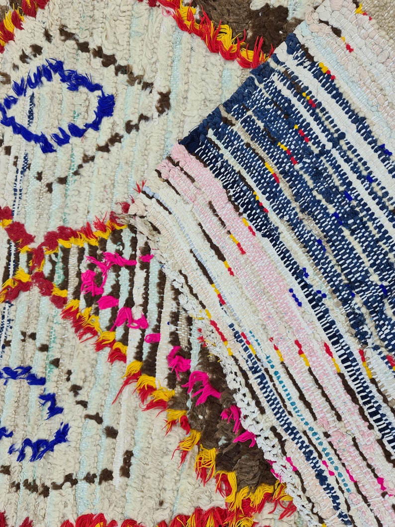 May include: A close-up of a colorful Moroccan rug with a white background and a variety of colors including blue, pink, yellow, and red. The rug is made of wool and has a hand-woven texture.