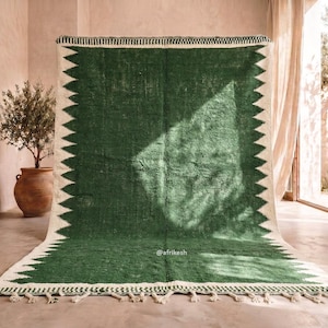 May include: A large, rectangular green rug with a white zigzag border and fringe. The rug has a textured appearance and is displayed indoors. The rug's design is simple yet striking, making it a focal point in any room.