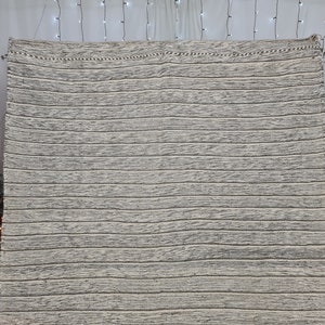 Puede incluir: Una alfombra tejida a rayas blancas y grises con un brillo sutil. La alfombra tiene un dise&ntilde;o simple y moderno y ser&iacute;a una gran adici&oacute;n a cualquier hogar.