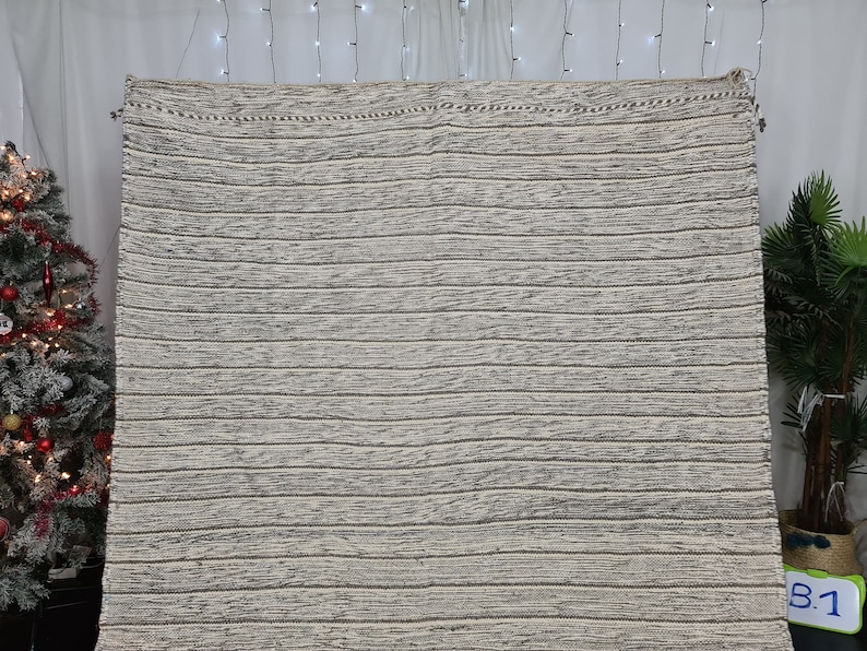 Puede incluir: Una alfombra tejida a rayas blancas y grises con un brillo sutil. La alfombra tiene un dise&ntilde;o simple y moderno y ser&iacute;a una gran adici&oacute;n a cualquier hogar.