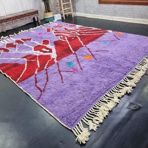 May include: A purple and red Moroccan rug with a geometric design and white fringe. The rug has a variety of colors, including orange, blue, and green.
