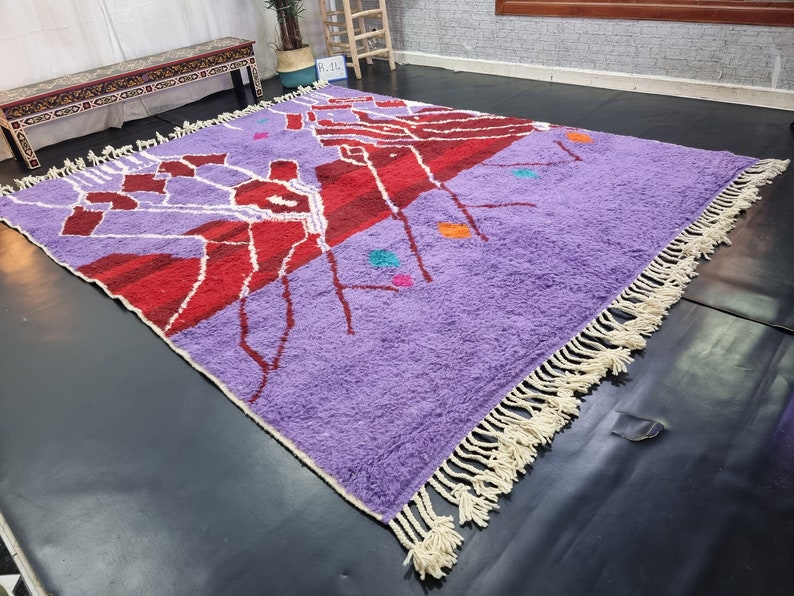 May include: A purple and red Moroccan rug with a geometric design and white fringe. The rug has a variety of colors, including orange, blue, and green.