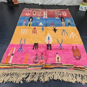 May include: A colorful Moroccan rug with a geometric pattern and fringe. The rug has a red, blue, yellow, and pink color scheme.