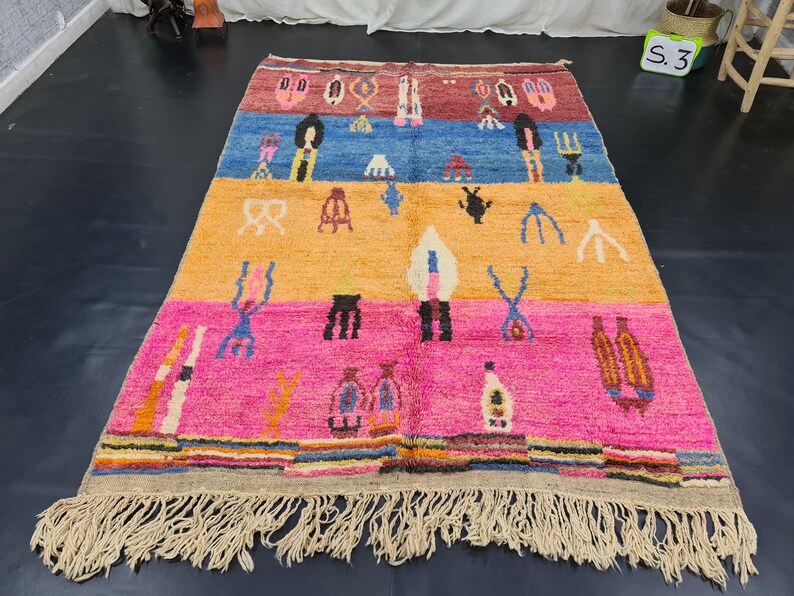 May include: A colorful Moroccan rug with a geometric pattern and fringe. The rug has a red, blue, yellow, and pink color scheme.