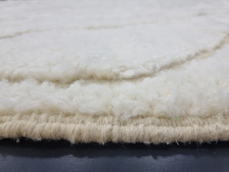 May include: Close-up of the edge of a white and beige shag rug. The rug has a thick, fluffy texture and a woven edge.