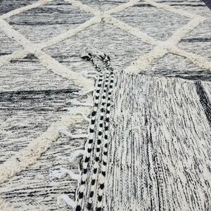 Op de afbeelding: Zwart-wit tapijt met een ruitpatroon en franjes. Het tapijt is gemaakt van een zacht, getextureerd materiaal.
