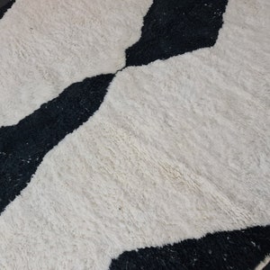 May include: Black and white geometric patterned rug with a fluffy texture. The rug has a wavy design with black and white stripes.
