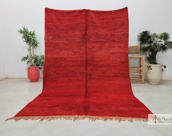 May include: A red Moroccan rug with a fringe border. The rug is made of wool and has a hand-woven texture.