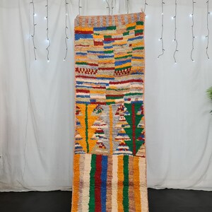 May include: A colorful Moroccan rug with geometric patterns in shades of red, blue, green, yellow, and orange. The rug is woven with a variety of textures and has a fringe on the bottom.
