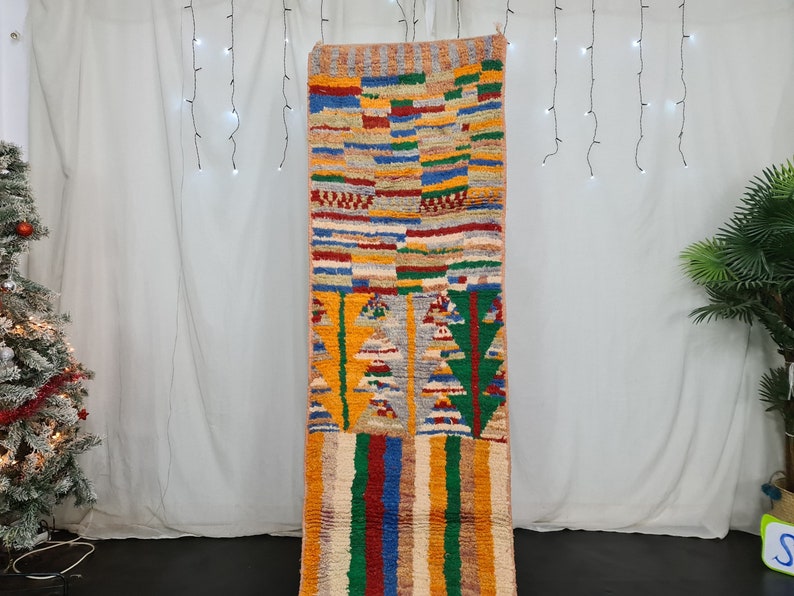 May include: A colorful Moroccan rug with geometric patterns in shades of red, blue, green, yellow, and orange. The rug is woven with a variety of textures and has a fringe on the bottom.