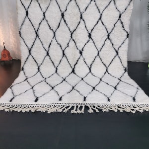 May include: White and black Moroccan rug with a diamond pattern and fringe. The rug is made of wool and is approximately 5 feet long.