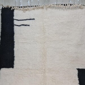 May include: A white and black Moroccan rug with a geometric design. The rug has a fringe border and is made of wool.