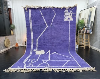 May include: A large, rectangular, purple and white Moroccan rug with a geometric pattern. The rug has a fringe border.