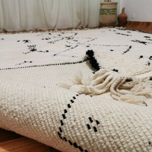 May include: A white and black Moroccan rug with a geometric pattern and fringe. The rug is made of wool and has a soft texture.