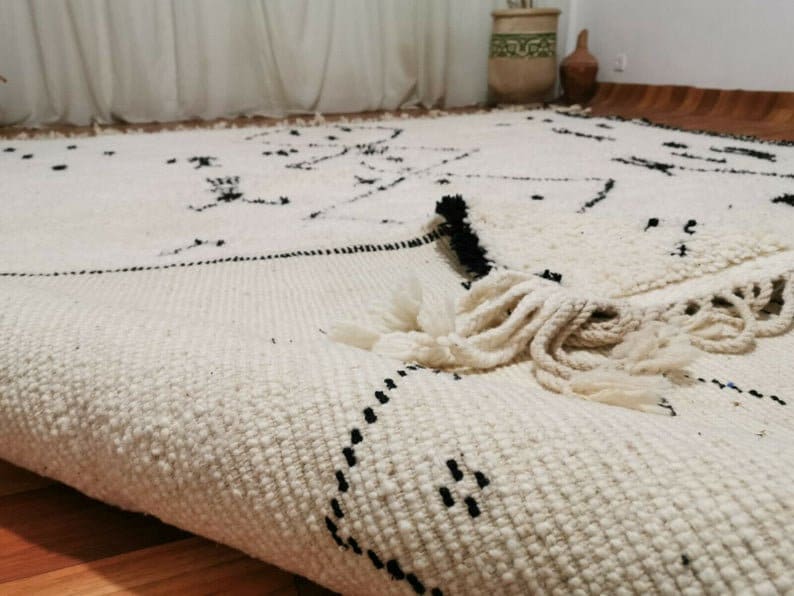 May include: A white and black Moroccan rug with a geometric pattern and fringe. The rug is made of wool and has a soft texture.