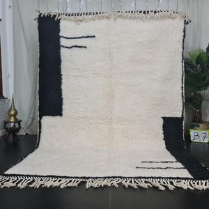 May include: A white and black Moroccan rug with a geometric design. The rug has a fringe border and is made of wool.