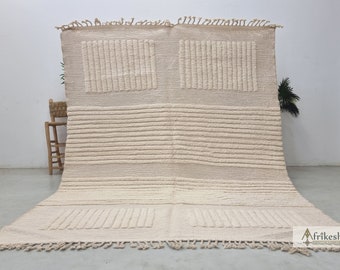 May include: A cream-colored woven rug with a textured pattern. The rug has a fringe border and is made of natural fibers.