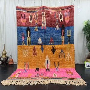May include: A colorful Moroccan rug with geometric patterns in shades of red, blue, orange, and pink. The rug has a fringe border and is hanging on a wall.