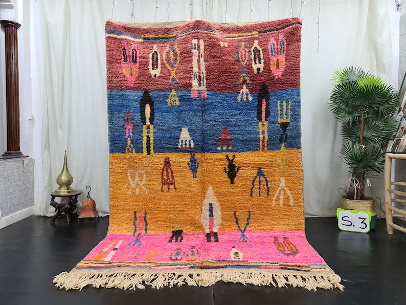 May include: A colorful Moroccan rug with geometric patterns in shades of red, blue, orange, and pink. The rug has a fringe border and is hanging on a wall.