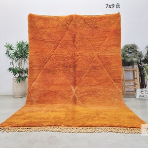 Puede incluir: Una alfombra marroquí grande de color naranja con un patrón de diamantes. La alfombra mide 7x9 pies y tiene un borde de flecos.