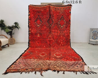 May include: A large, red Moroccan rug with a geometric pattern. The rug is 6.6 feet by 12.6 feet and has a fringe border.