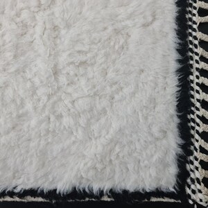 May include: White fluffy rug with a black and white fringe border.
