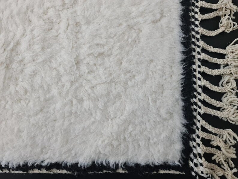 May include: White fluffy rug with a black and white fringe border.